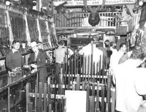 Hy Hunter behind the counter of his shop, examining Great Western single actions with the legendary Carbine Williams.